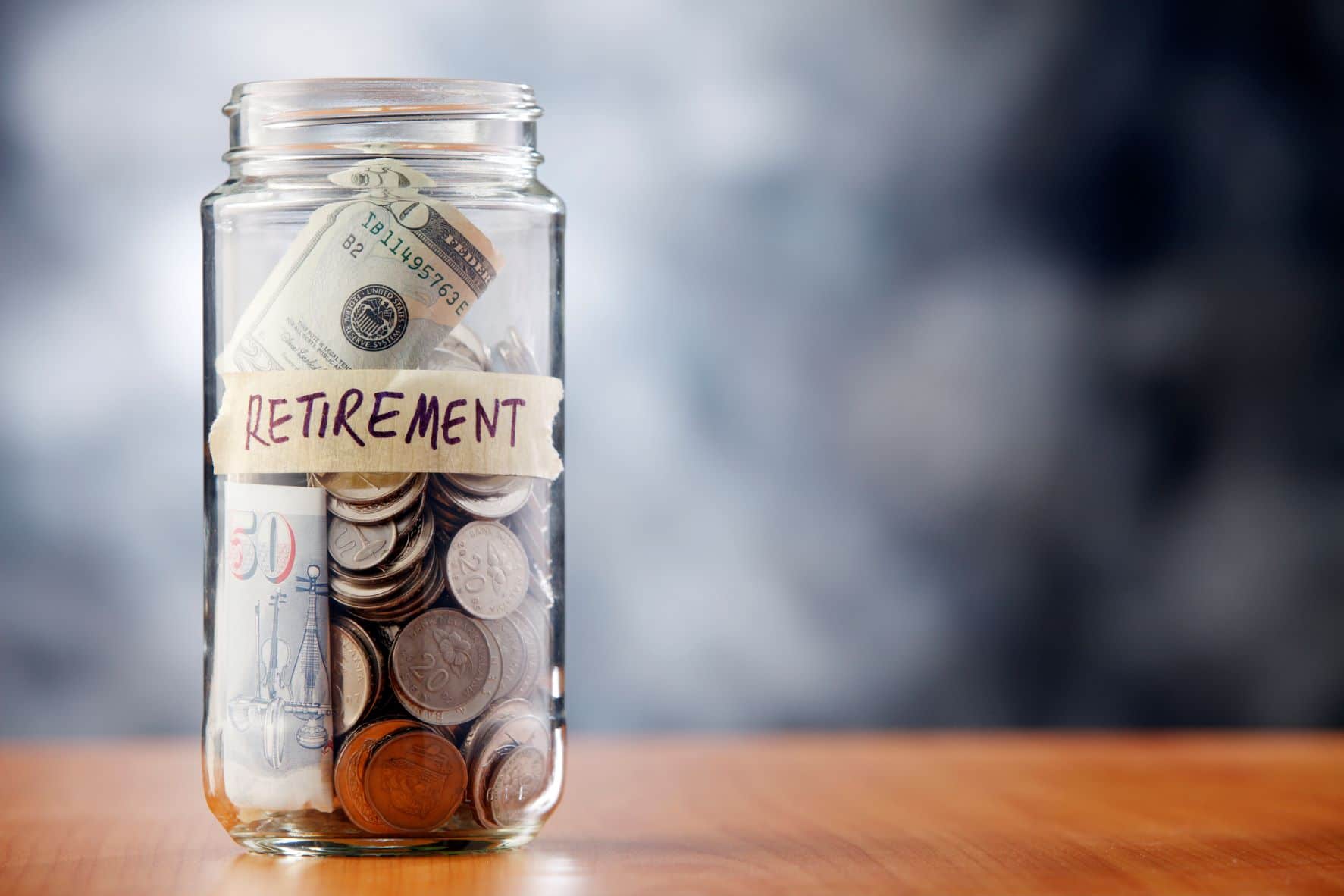 A glass jar labeled “retirement” filled with various coins and paper bills.