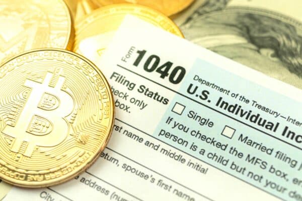 A physical representation of a Bitcoin sits on top of a tax form.