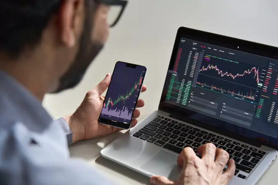 A man looking at a line graph of crypto prices on his laptop and phone.