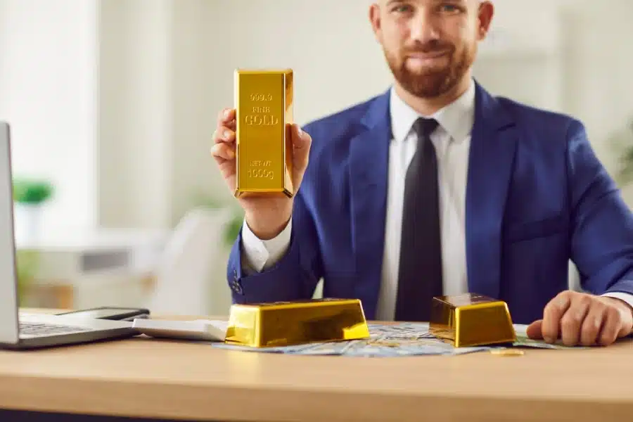 A young businessman holding a gold bar.