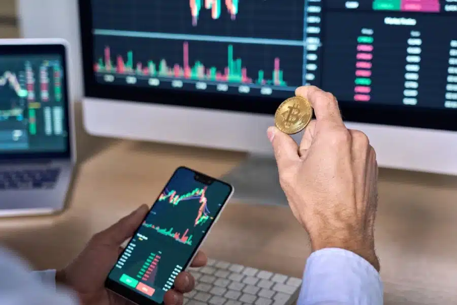 A trader looking a screens of the market, and holding a bitcoin.