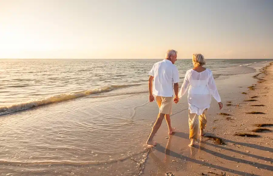 A retired couple walking on the beach.
